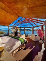 Un dormitorio amplio con una cama grande, vista a un lago y techo de cristal.