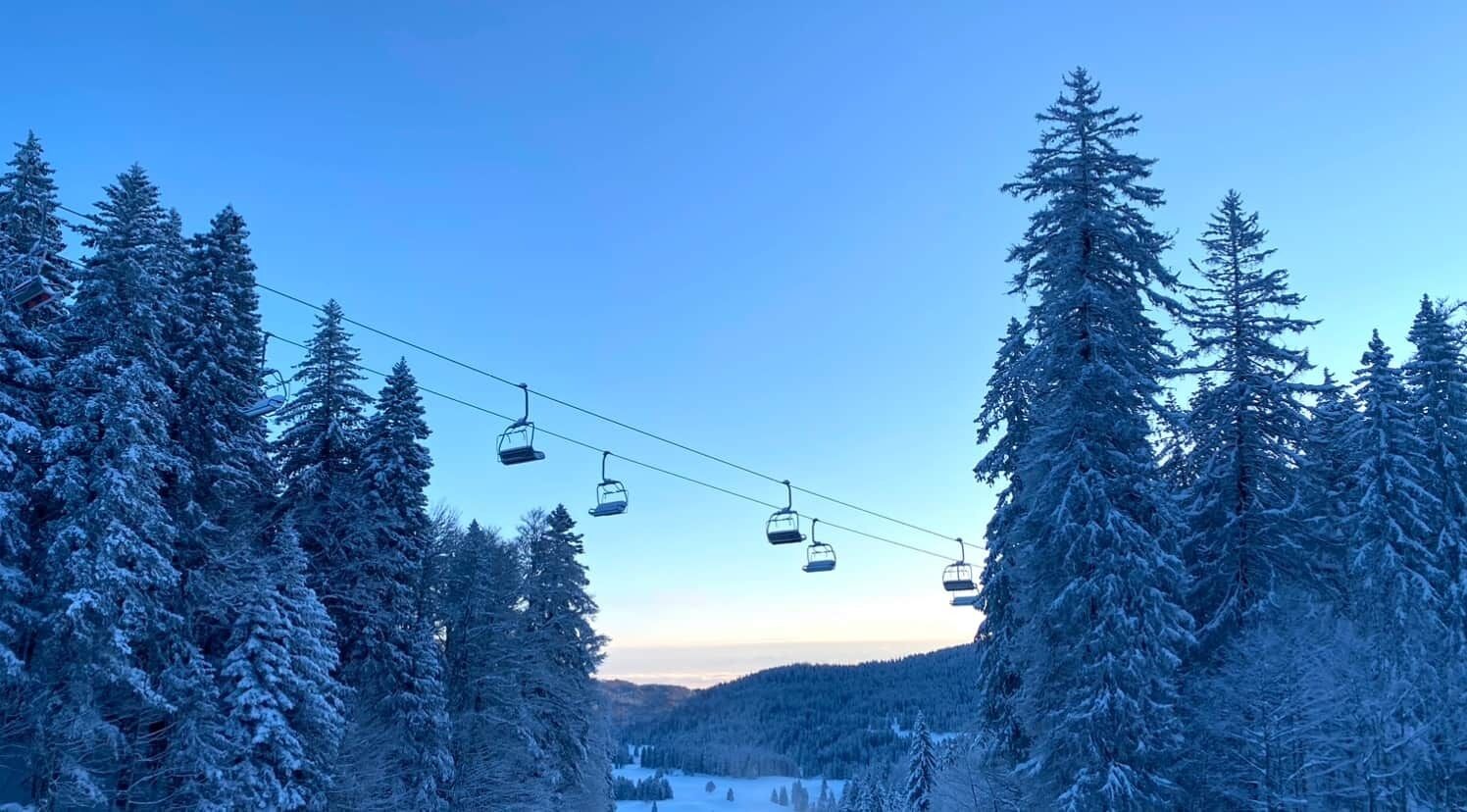 A ski lift with cabins suspended over a snowy forest.