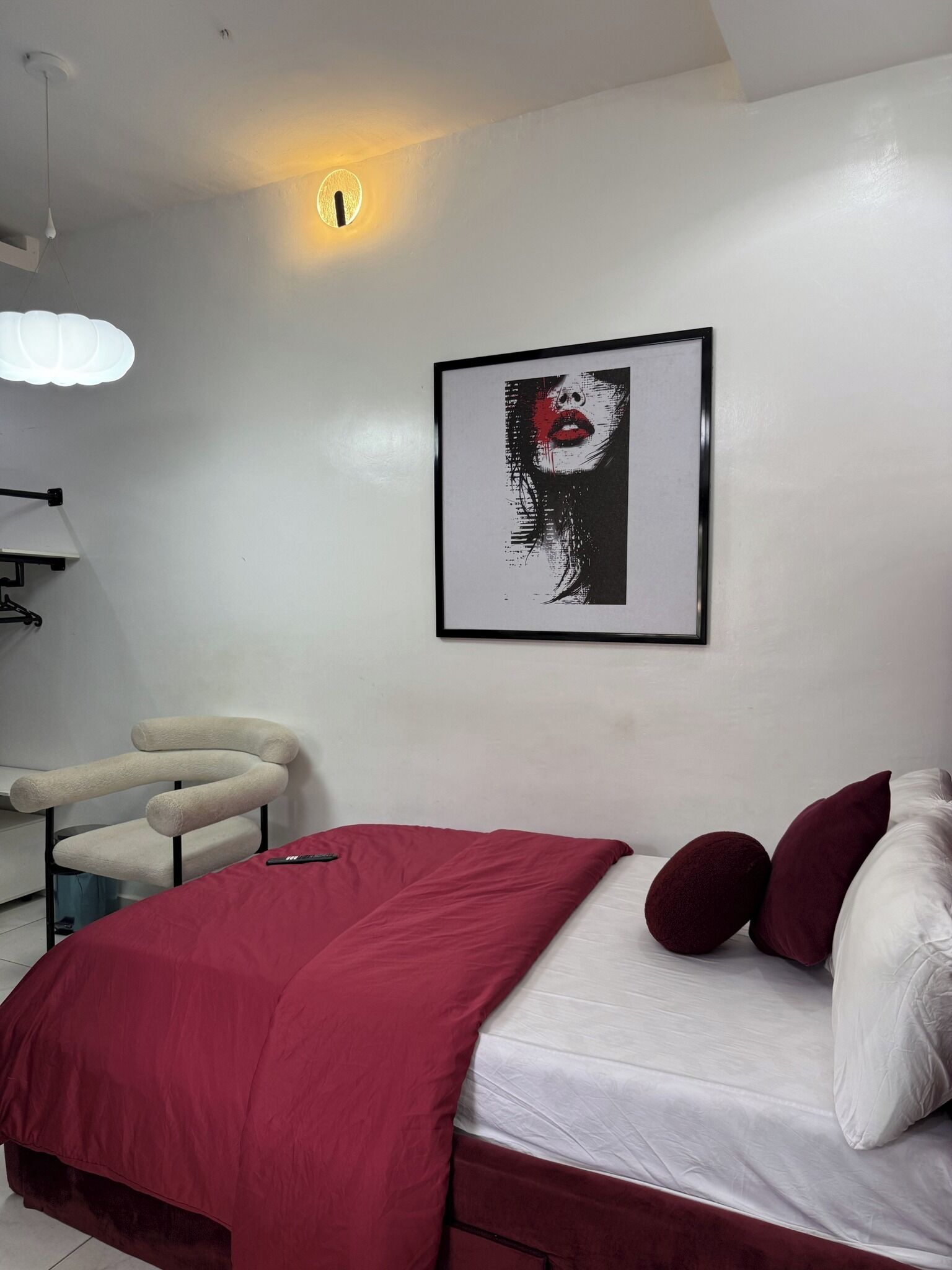 A modern bedroom with a bed, a chair, a framed artwork, and a ceiling light.