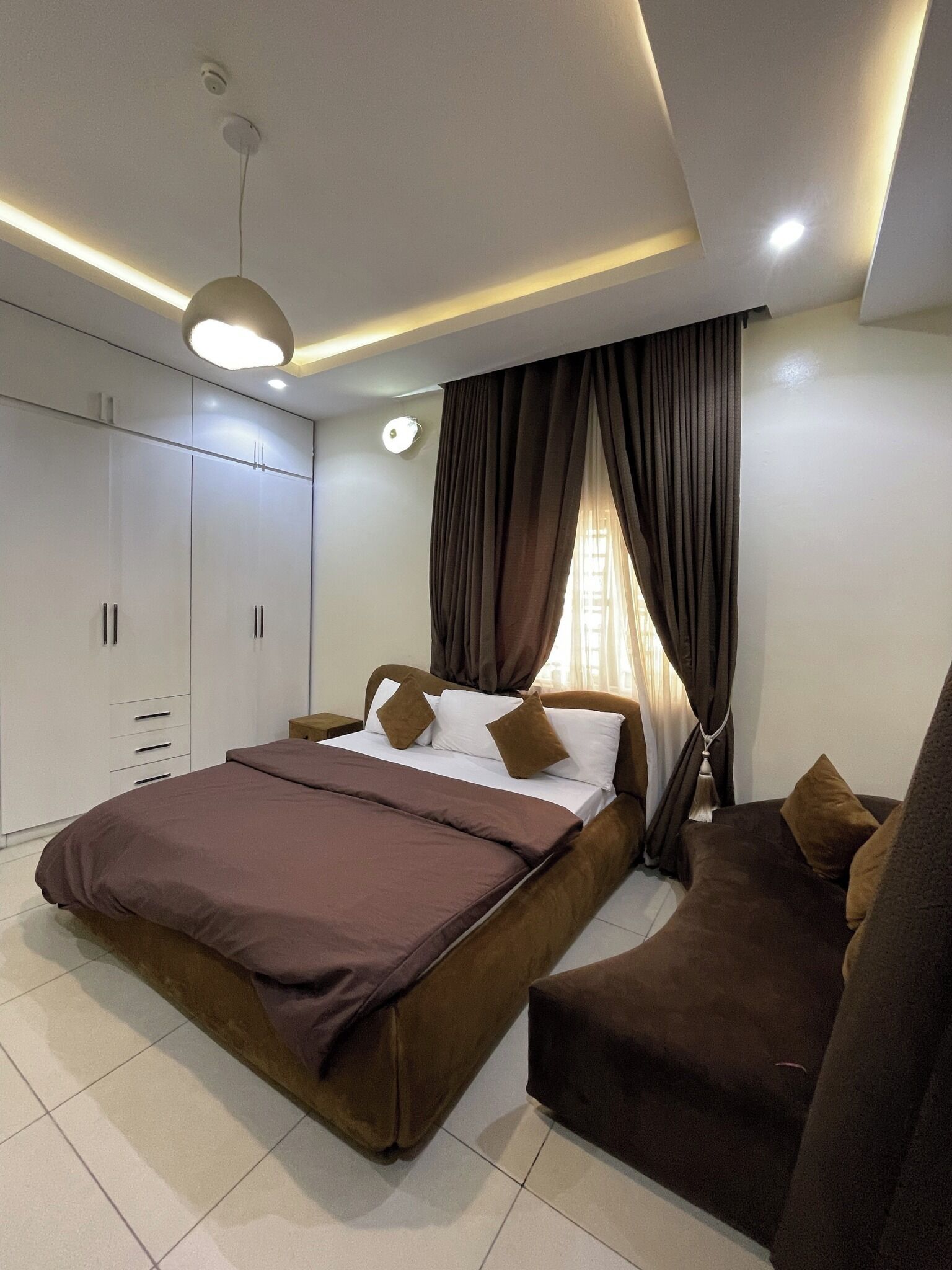 A modern bedroom with a bed, a sofa, a wardrobe, and a ceiling light.
