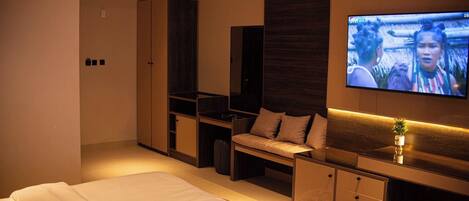 Una habitación de hotel moderna con una cama grande, un televisor montado en la pared, un sofá y un escritorio con cajones.
