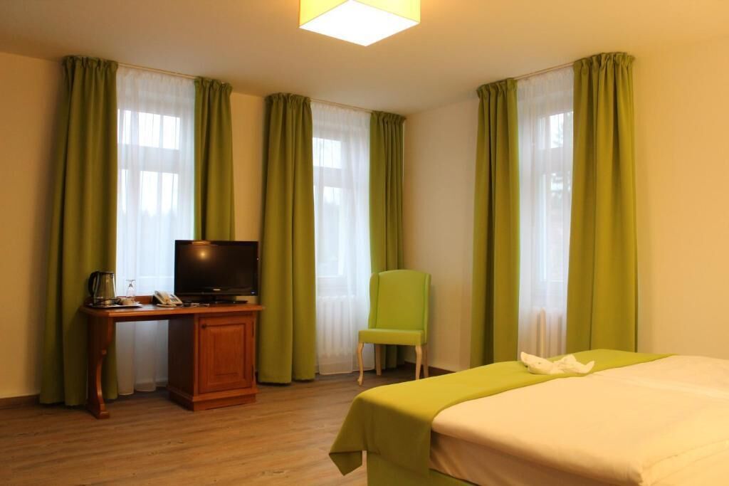 A hotel room with a bed, a desk with a television, a chair, and curtains.
