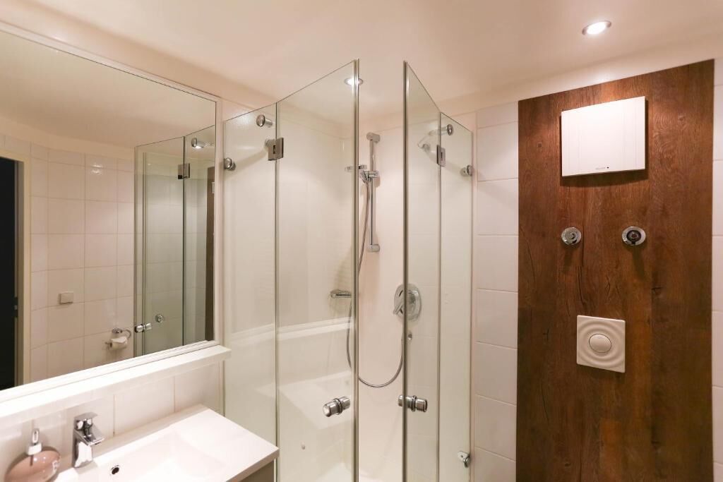 A modern bathroom with a glass-enclosed shower, a white sink, and a wooden panel wall.