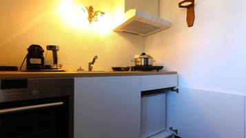 A compact kitchen with a coffee maker, a pot on the stove, and a wall-mounted knife.