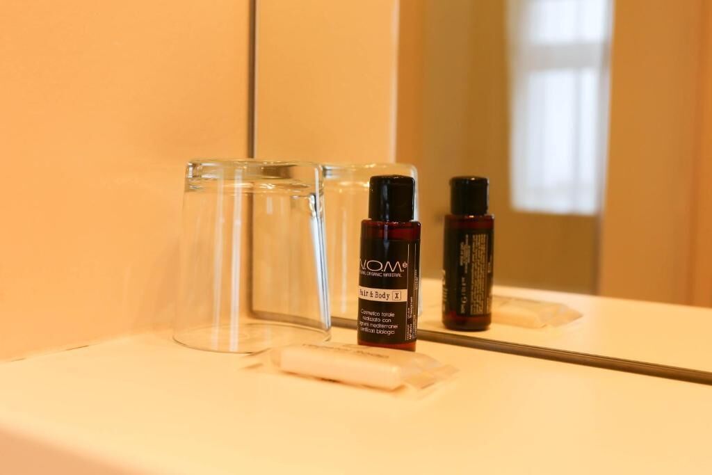 A bathroom with a mirror, a bottle of hair and body care product, and a clear glass.