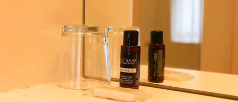 Un baño con espejo, un producto de cuidado para cabello y cuerpo, y una copa de vidrio.