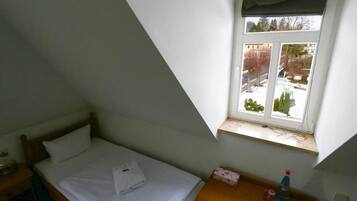 A small, single-bed room with a window overlooking a snowy landscape.