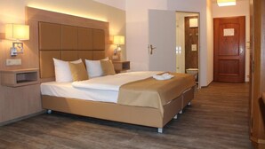 Ein Hotelzimmer mit einem großen Bett, Nachttischlampen, einem hölzernen Kopfteil, einer Holztür und einem Holzboden.