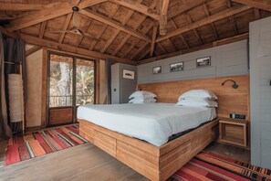 A wooden-framed bedroom with a large bed, a window, and a small bedside table.