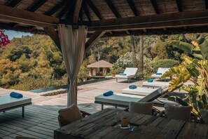 Eine Holzterrasse mit Liegestühlen und einem Tisch, mit Blick auf einen Pool und üppiges Grün.