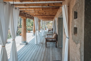 A covered outdoor area with wooden beams, white curtains, and a bench.