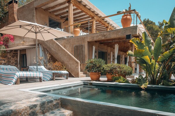 A pool area with lounge chairs, a pergola, and potted plants.