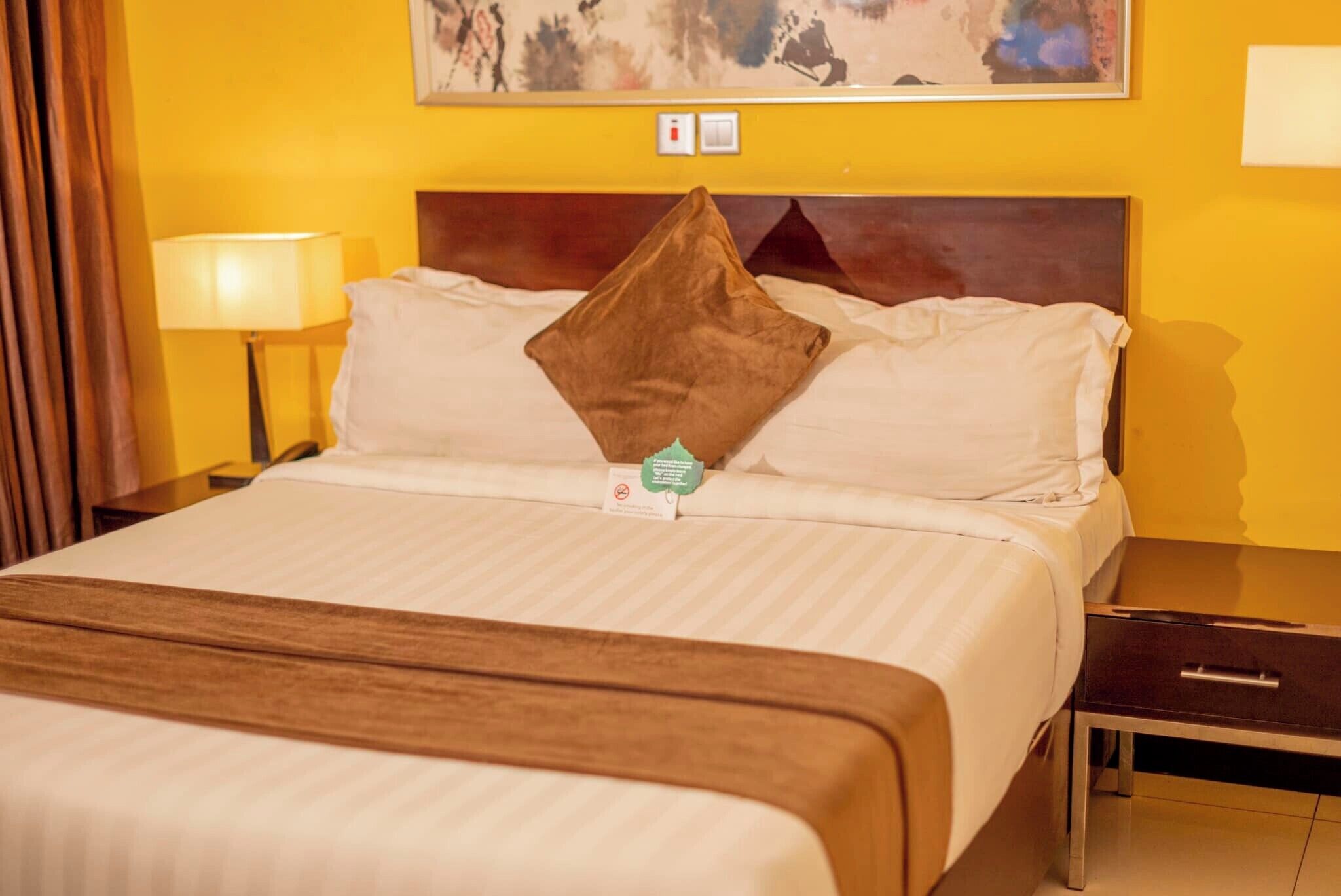 A hotel room with a bed, a nightstand, a lamp, and a painting on the wall.