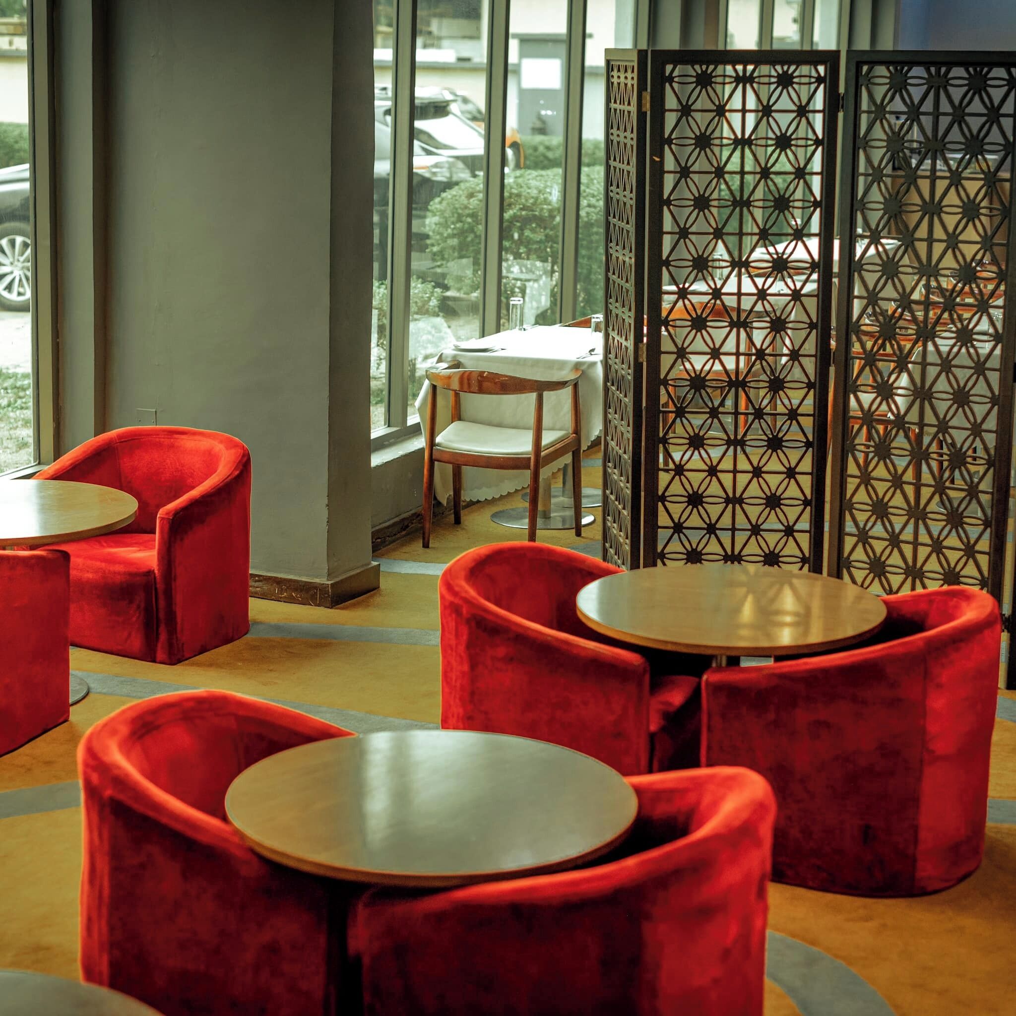 A seating area with red upholstered chairs and round tables, a wooden chair, and a decorative partition with geometric patterns.