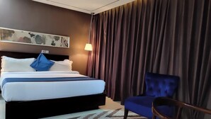 A hotel room with a bed, a chair, a lamp, and a painting on the wall.