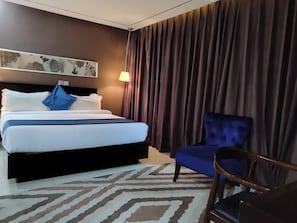 A hotel room with a bed, a chair, a lamp, and a painting on the wall. - The Addrex Hotel And Suites (Aba)