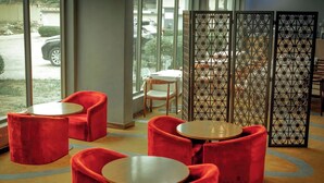 A seating area with red chairs and round tables, a view through large windows, and a decorative partition.