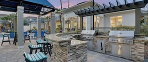 An outdoor kitchen area with a grill, bar seating, and a poolside setting. - Stylish 2BR Retreat Near Midtown Tampa (Westchase)
