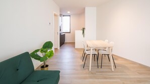 Un salon moderne avec un canapé vert, une table à manger avec des chaises, une plante en pot et une vue sur la cuisine.