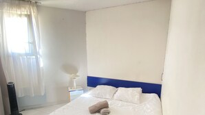 Een hotelkamer met een groot bed, een nachtkastje met een lamp, een raam met dunne gordijnen en een elektrische verwarming.