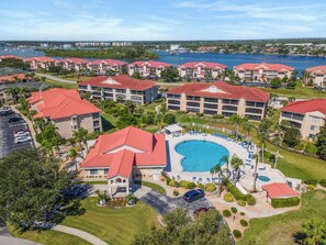 A resort with multiple buildings, a central swimming pool, and a marina in the background. - 🚲 Bouchelle Island 202 | Intracoastal Views | Screened Porch & Beach Cruisers (New Smyrna Beach)