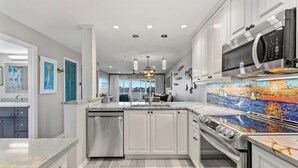 Una cucina moderna con mobili bianchi, elettrodomestici in acciaio inossidabile e una parete di fondo con decoro a mosaico.