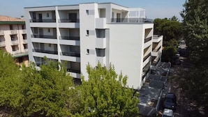 A multi-story building with balconies, a parking area, and surrounding greenery. - Modern Apartment 300m From the sea (San Michele al Tagliamento)
