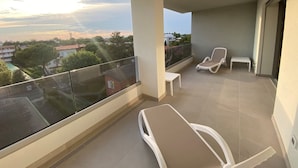 Ein Balkon mit zwei weißen Lounge-Sesseln, einem kleinen Tisch und Blick auf eine Wohngegend mit Bäumen und Häusern.