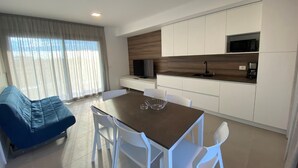 Una cocina moderna con armarios blancos, una mesa de comedor con sillas, un sofá azul y un ventanal con cortinas.