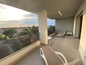 Ein Balkon mit zwei weißen Lounge-Sesseln, einem kleinen Tisch und Blick auf eine Wohngegend mit Bäumen und Häusern.