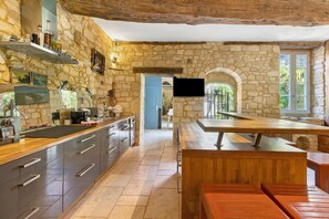 A stone-walled kitchen with a wooden countertop, a dining area with benches, and a television mounted on the wall. - Holiday Home “La Maison de Marie” with Shared Terrace, Wi-Fi & Air Conditioning (Domme)