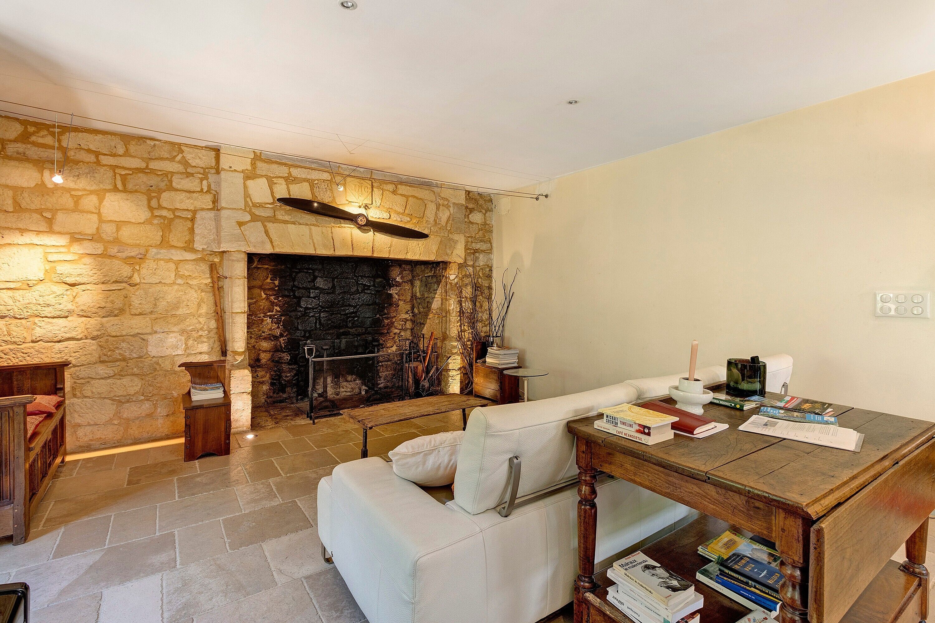 A cozy living room with a stone fireplace, a white sofa, and a wooden coffee table with books.
