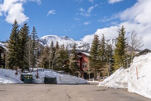 A red building with a stone facade, surrounded by snow-covered ground and trees, with a mountain in the background. - Mountain View Snowcreek Condo with Community Hot Tub and Fireplace (Mammoth Lakes)