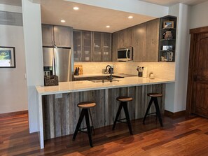 Eine moderne Küche mit Marmorarbeitsplatte, Edelstahlgeräten und Holzbarhocker.