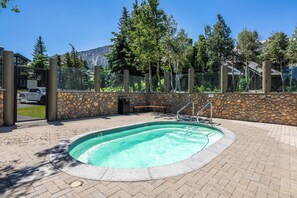 A swimming pool with a stone wall and metal fence, surrounded by trees and a mountain in the background. - Mountain View Snowcreek Condo with Community Hot Tub and Fireplace (Mammoth Lakes)