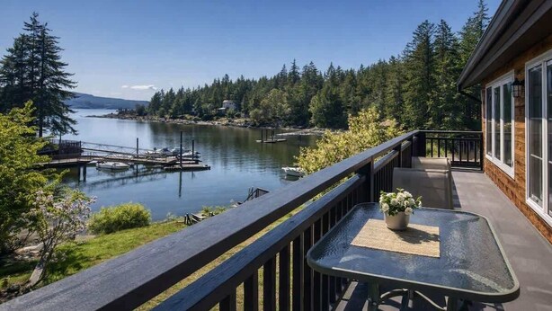 A balcony with a view of a lake, dock, and forest.