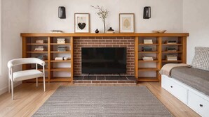 A living room with a fireplace, bookshelves, a TV, a white chair, and a bed.