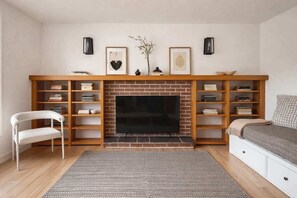 A living room with a fireplace, bookshelves, a TV, a white chair, and a bed.
