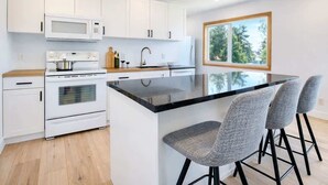 A modern kitchen with white cabinets, a black countertop, a built-in oven, a microwave, and a large island with bar stools.