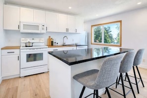 A modern kitchen with white cabinets, a black countertop, a built-in oven, a microwave, and a large island with bar stools.
