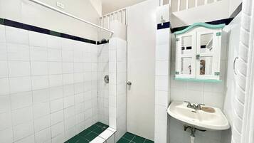 A bathroom with white tiles, a green-tiled shower floor, a white sink, and a mirror with a glass shelf above it.