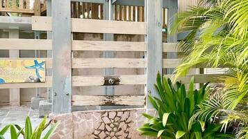A wooden gate leading to a building with a stone wall and tropical plants.