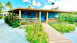 Ein Gebäude direkt am Strand mit einer überdachten Terrasse, einem Holzdeck und üppiger Bepflanzung.