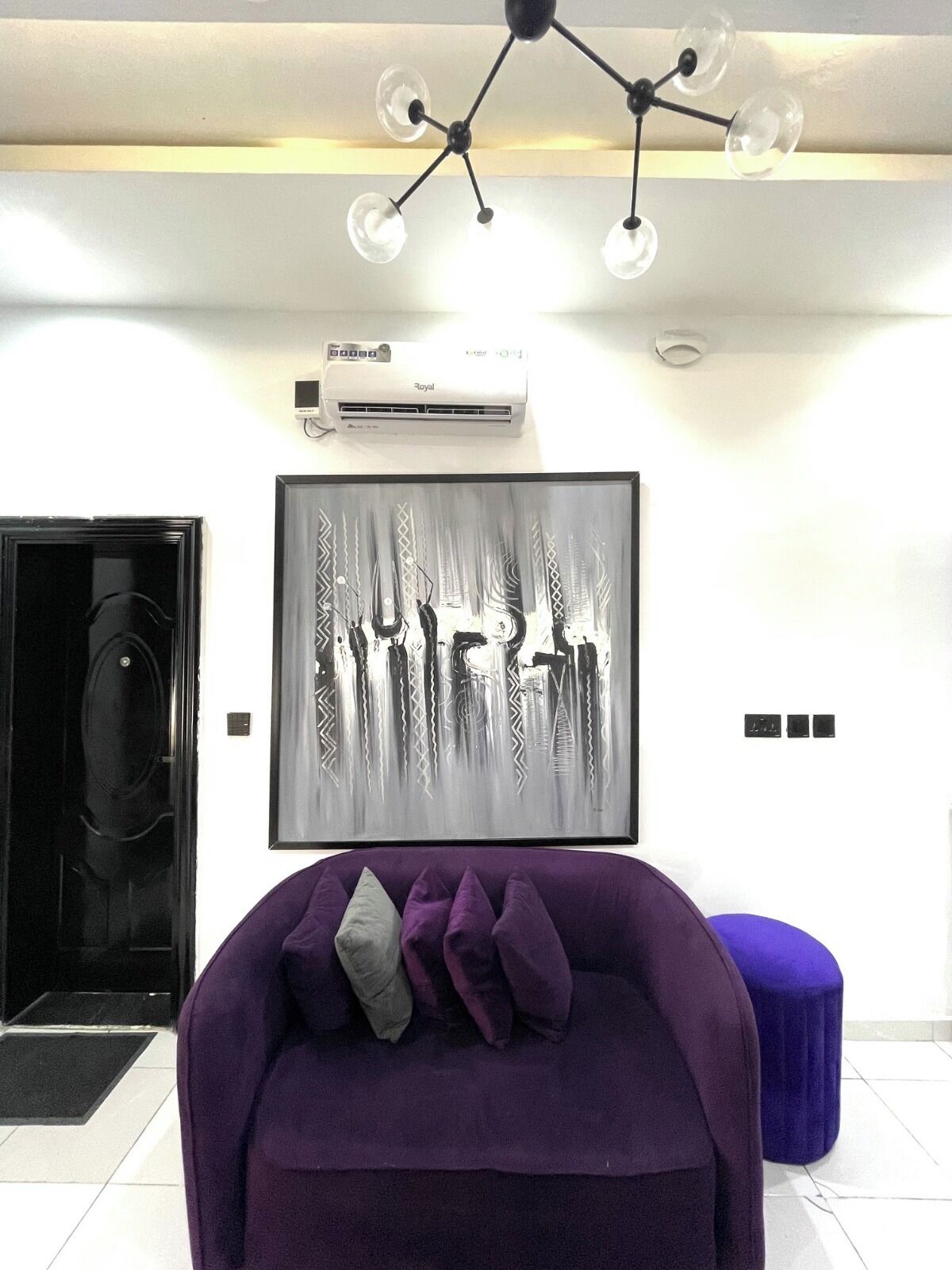 A modern living room with a purple sofa, a framed abstract artwork, a ceiling light fixture, and an air conditioning unit.