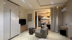 Quarto de hotel moderno com cama, sofá, área de refeições e cozinha compacta.