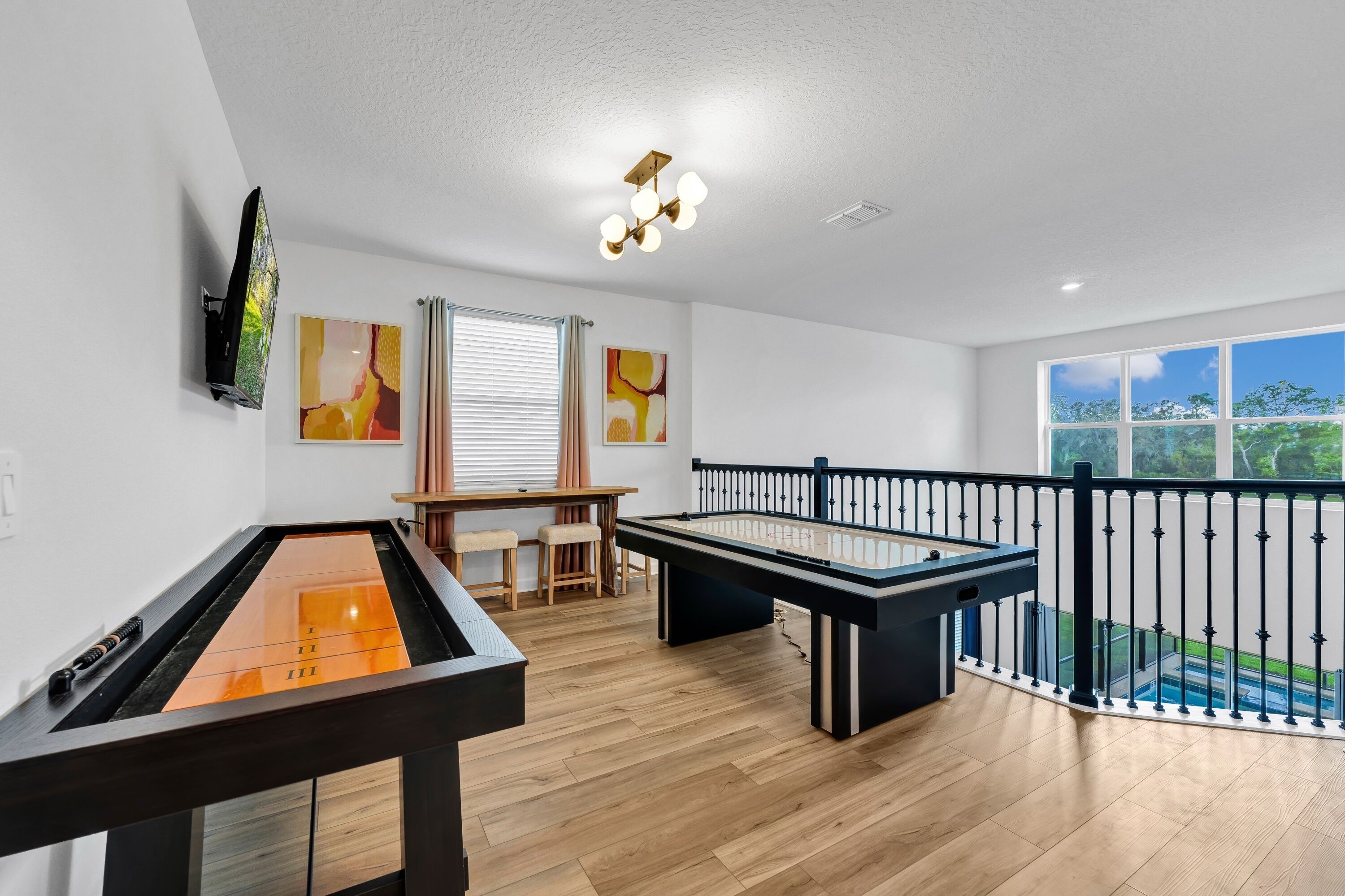 Une table de billard, un baby-foot, un téléviseur et des œuvres d’art sur un mur blanc.