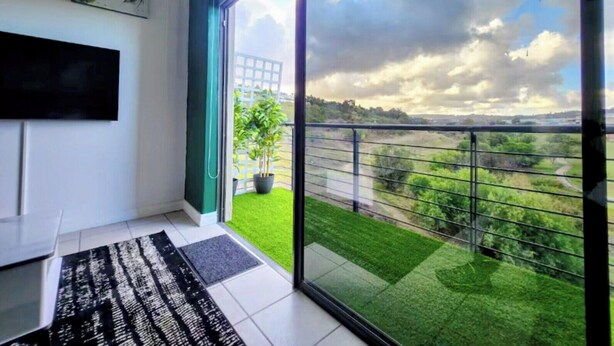 Un salón moderno con un gran ventanal corredera que da a un balcón con vistas a un paisaje verde y un cielo nublado.