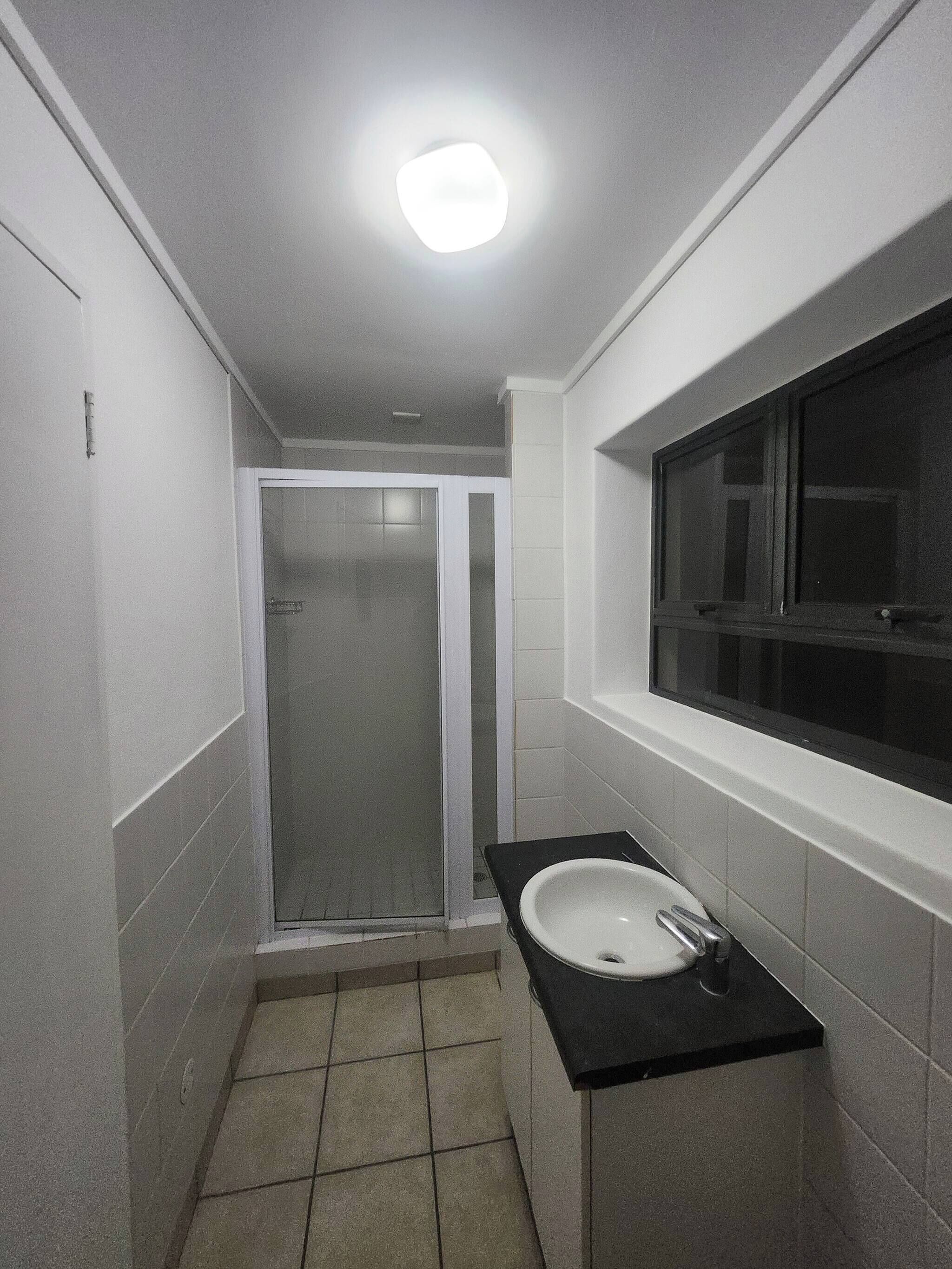 Ein Badezimmer mit Dusche, Waschbecken und Fenster.