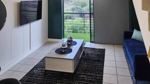 Una sala de estar moderna con un televisor de pantalla plana, una mesa de centro, un sofá, una escalera y un balcón con vistas.
