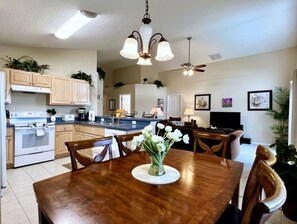 A dining area with a wooden table, chairs, a vase of flowers, a ceiling fan, and kitchen cabinets in the background. - Arcade Game Night! Epic Value! Near Parks! 335 (Davenport)